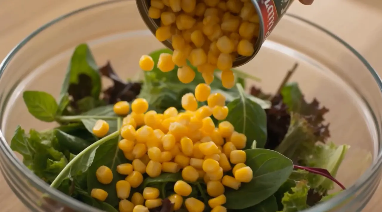 Frame from the Puidor AI film: sweetcorn falling into a glass bowl of spinach, soft morning light